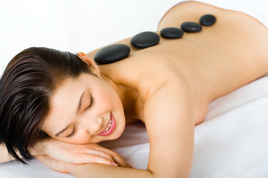 Photo of young happy girl lying at cosmeticians with spa stones along her back enjoying cosmetic procedure